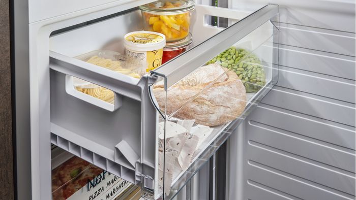 Ein Siemens Einbau-Gefriergerät mit geöffneter Schublade. In der Schublade sind Brot, Eis und andere Lebensmittel. 