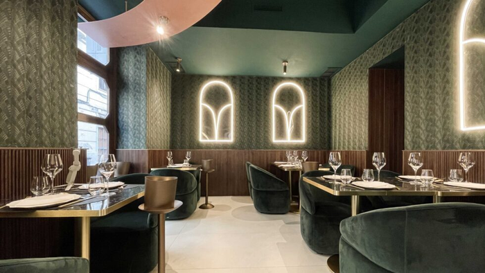 Elegante restaurante interior con asientos de terciopelo verde, acentos de madera e iluminación de neón arqueada.