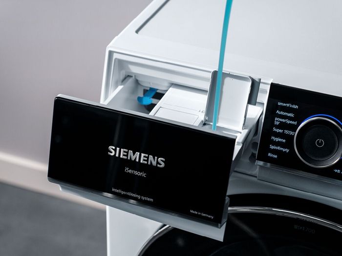 Gros plan sur le bac &agrave; lessive d'un lave-linge Siemens iSensoric en train d'&ecirc;tre rempli de lessive liquide, avec le panneau de commande num&eacute;rique.