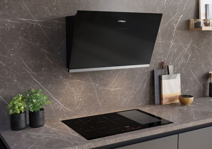 Cappa da parete installata sopra un piano cottura a induzione Siemens, in una cucina con top e rivestimento effetto marmo