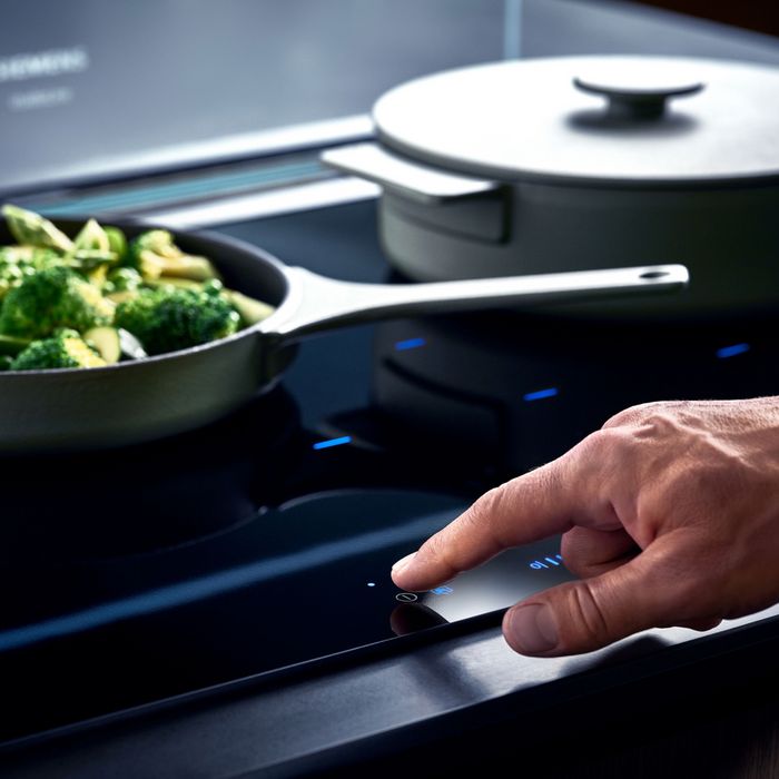 Primo piano di un piano cottura a induzione con pentole in uso e mano che regola i comandi touch illuminati