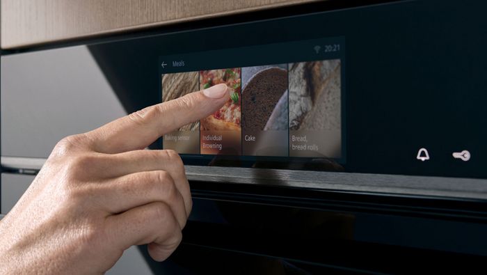 Mano che seleziona sul display il programma di cottura di un forno multifunzione Siemens