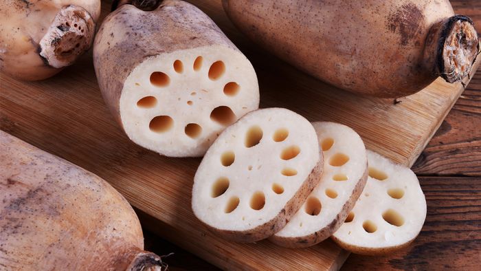 Freshly sliced lotus roots displaying round holes on a wooden cutting board.