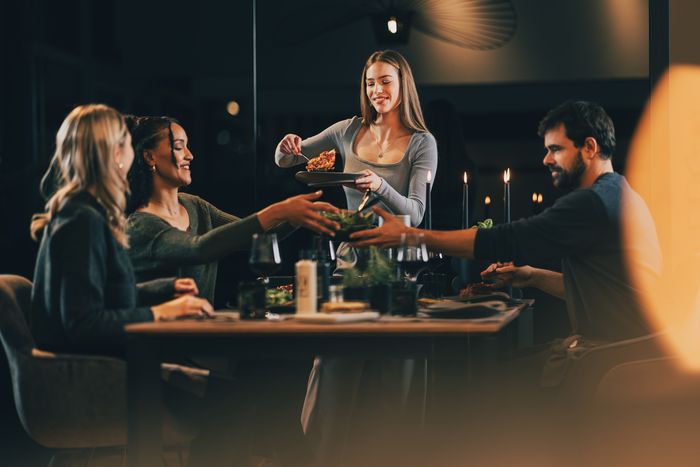 Gruppo di amici a cena mentre una donna serve un piatto di pasta