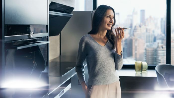A woman using her phone in the kitchen next to a Siemens oven.