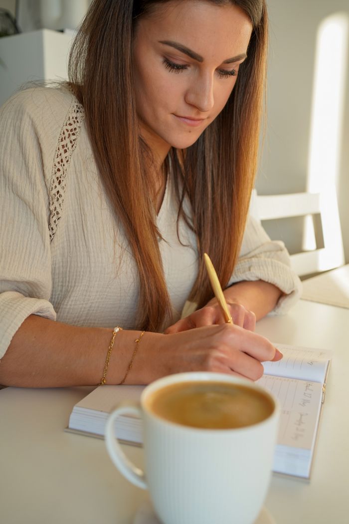 Gros plan sur Laura, assise à une table, en train d'écrire son journal. Une grande tasse de café se trouve devant elle. C'est ainsi que le café contribue à sa routine de santé mentale.