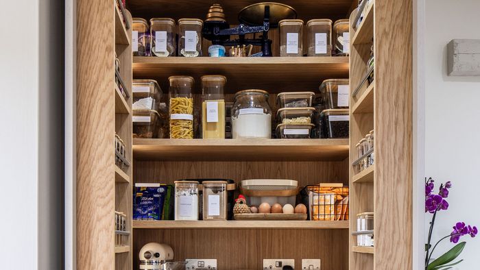 A pantry with a wooden door and shelves, neatly organized with various food items and kitchen supplies.