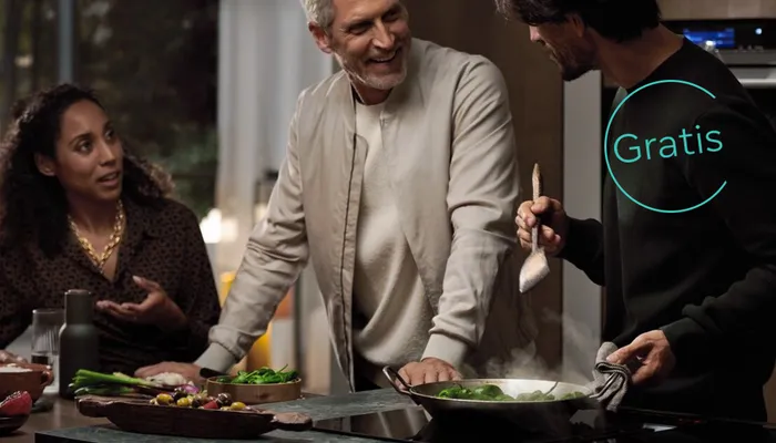 En modern köksmiljö med färska grönsaker och en fräser panna, som framhäver en livlig matlagningsatmosfär bland tre personer.