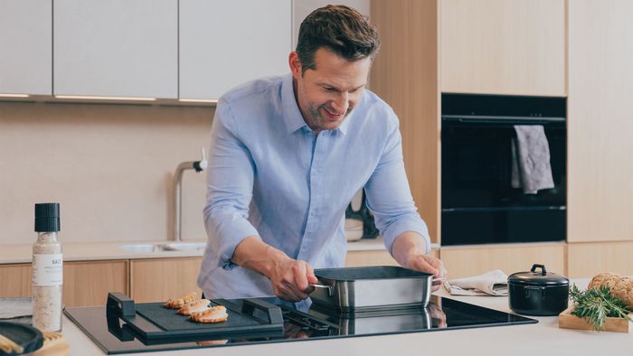 Mann kocht in moderner Küche mit Siemens Backofen und Induktionskochfeld.