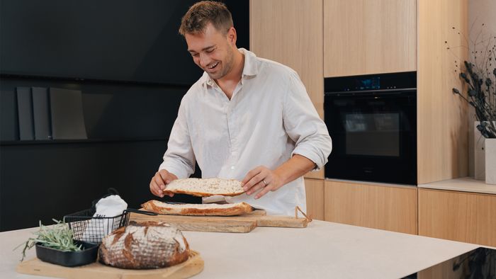 Mann in Küche mit Siemens Backofen, bereitet ein Baguette zu.