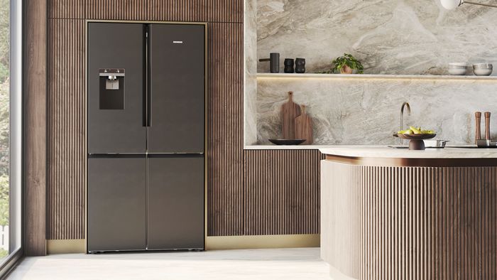 Et moderne sort k&oslash;leskab med indbygget vanddispenser, placeret i et stilfuldt k&oslash;kken med tr&aelig;detaljer og elegant dekoration p&aring; bordpladen.