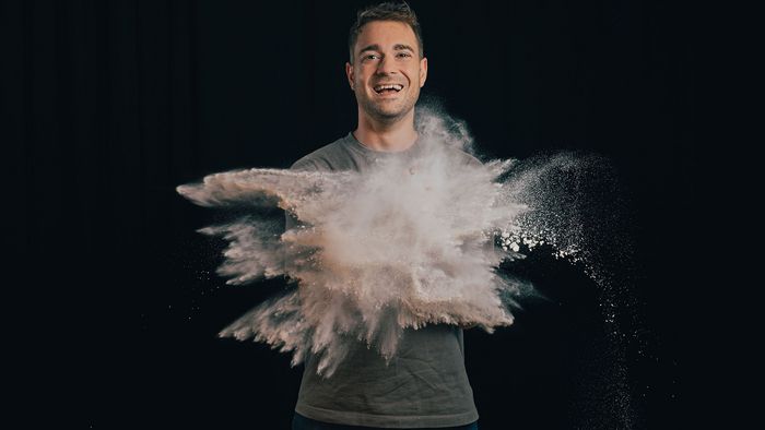 Jo Semola, der Brotfluencer, in dunklem Raum, lächelnd, mit explodierendem Mehl vor sich.