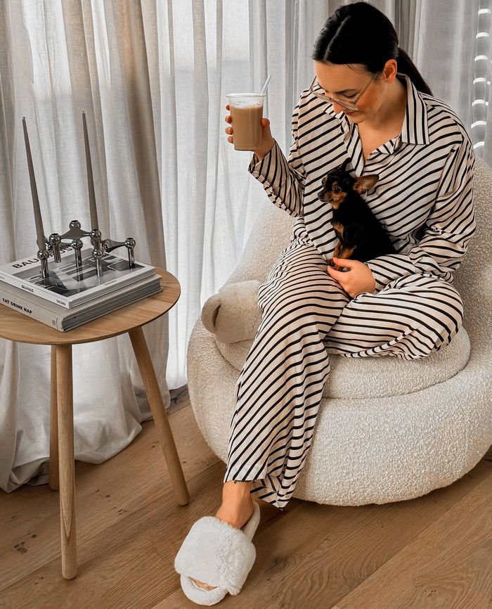 Laura zit in een fauteuil, een koffie in de ene hand, haar hondje op schoot. Haar favoriete koffiemomenten ontvouwen zich thuis, omringd door haar dierbaren.