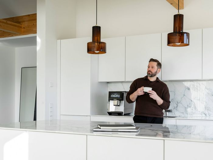 Dominik in zijn witte keuken met een Flat White in zijn handen. Telkens als hij hem 's ochtends drinkt, brengt zijn koffiemoment hem terug naar zijn allereerste Flat White in New York.