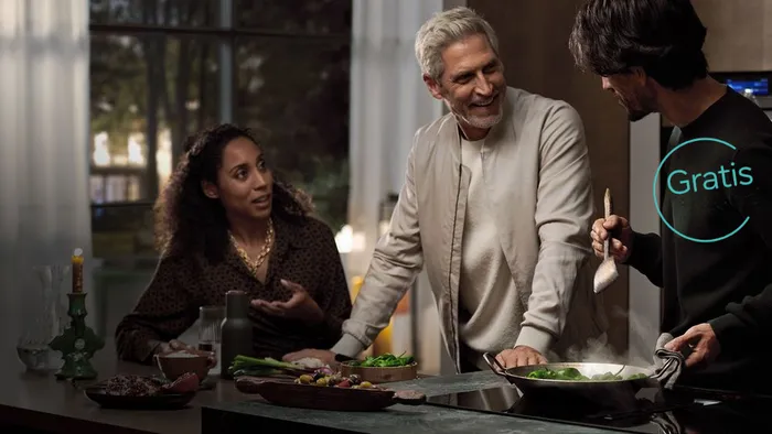 Tre personer tilbereder mat sammen på et kjøkken, smiler og samhandler.