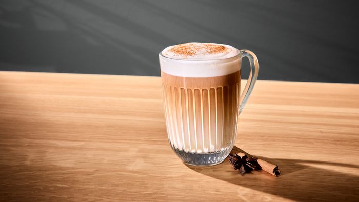 Un verre contenant un dirty chai latte  sur une surface en bois. Un b&acirc;ton de cannelle et de l'anis &eacute;toil&eacute; sont pos&eacute;s &agrave; c&ocirc;t&eacute;.