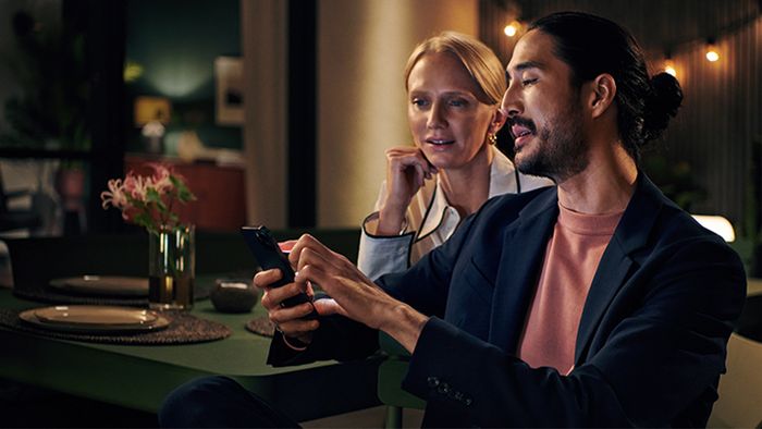 A man and woman seated at a table, both focused on their smartphones, engaged in their own digital worlds.