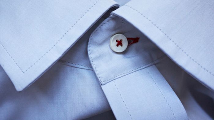 Primo piano del colletto e del primo bottone di una camicia formale azzurra.