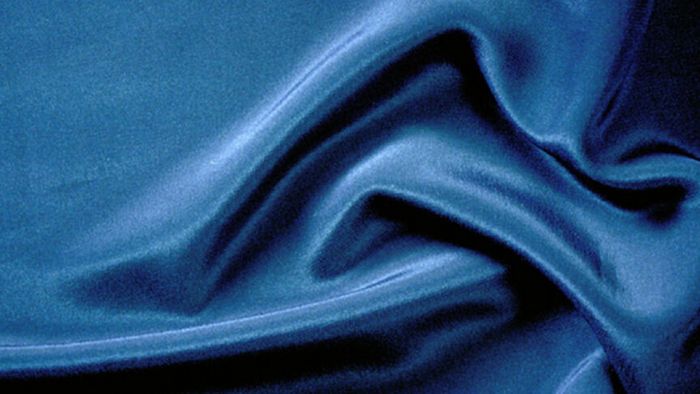 Primo piano di un drappo in seta blu scuro raccolto a formare pieghe lucide.