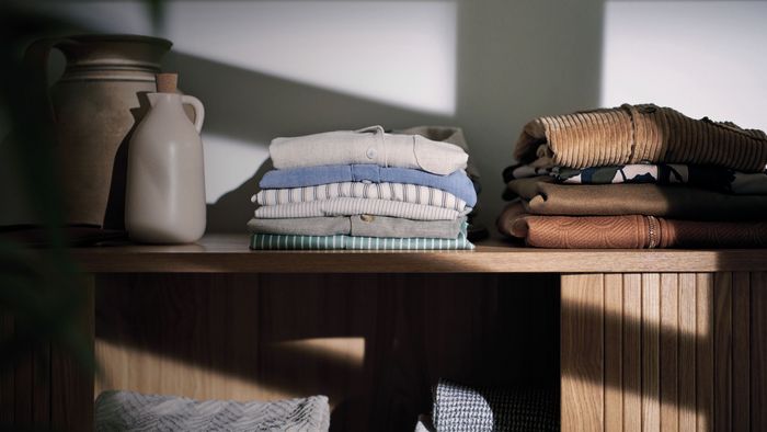 Pilhas de roupa rec&eacute;m-lavada, dobradas com cuidado, repousam numa prateleira de madeira.