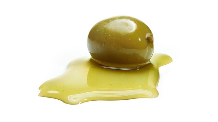 Eine grüne Olive liegt in einer Pfütze Öl.