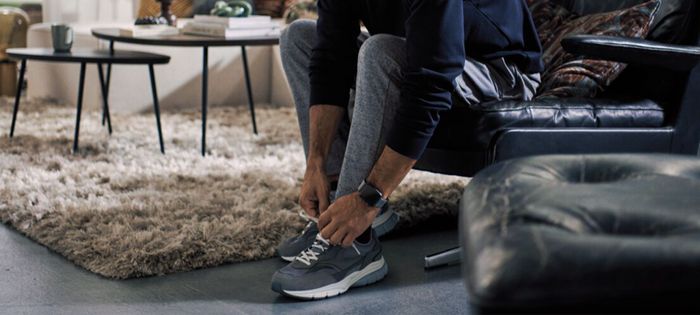 Ein sportlich angezogener Mann sitzt auf einem Stuhl und bindet die Schnürsenkel eines Paars sauberer blauer Laufschuhe.