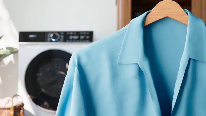 Ein knitterfreies, t&uuml;rkisfarbenes Hemd h&auml;ngt sauber auf einem Kleiderb&uuml;gel, im Hintergrund ist ein Vollwaschtrockner.