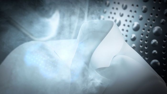 Nahaufnahme eines weissen Hemds in der Trommel einer Waschmaschine, umgeben von einer Wolke Reinigungsluft, die von der Maschine produziert wird.