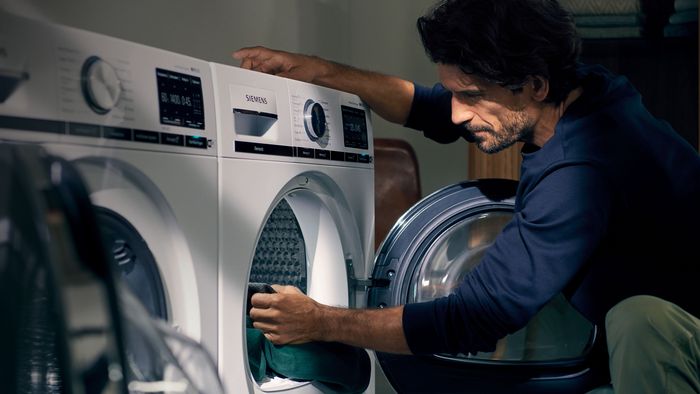 Ein Mann belädt seinen Trockner, während ihm die Sonne durch das Fenster ins Gesicht scheint