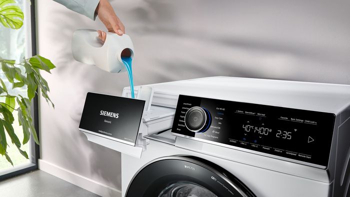 Eine Frauenhand gibt Waschmittel in die offene Schublade einer Waschmaschine.