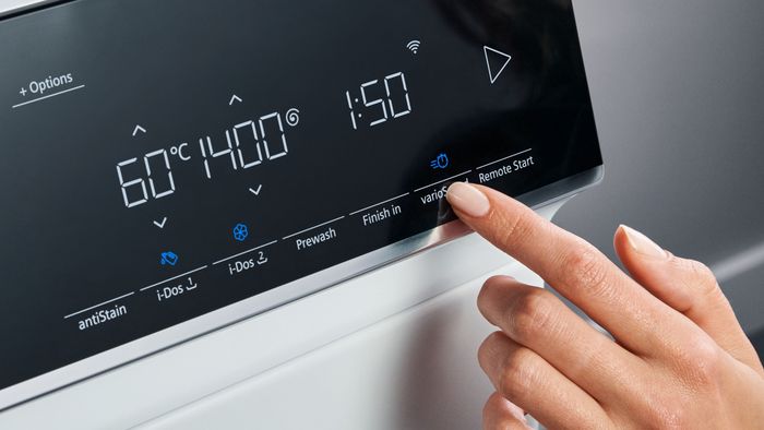 Eine Hand schwebt über den Einstellungen einer Waschmaschine, bereit, das richtige Programm für die Wäscheladung auszuwählen.