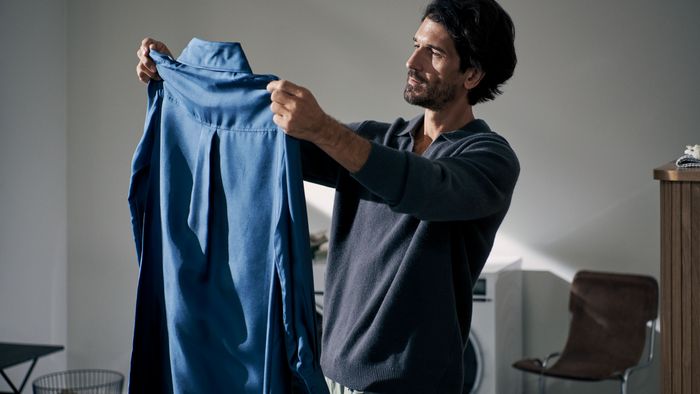 Ein Mann steht im Licht und hält ein blaues Hemd hoch, das so faltenfrei ist, dass es direkt angezogen werden kann.