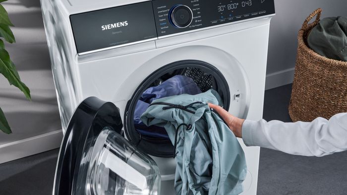 Einige hellblaue Kleidungsstücke werden zu einer kleinen Ladung in einer Waschmaschine hinzugefügt.