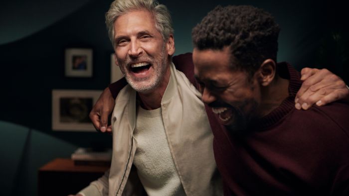 Twee mannen lachen terwijl ze met hun armen om elkaars schouders staan.