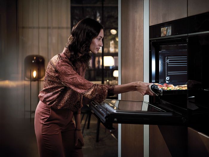 Donna in cucina che estrae una teglia di verdure dal forno da incasso Siemens