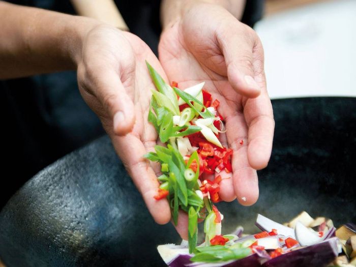 Mani che mettono le verdure in padella per cucinarle