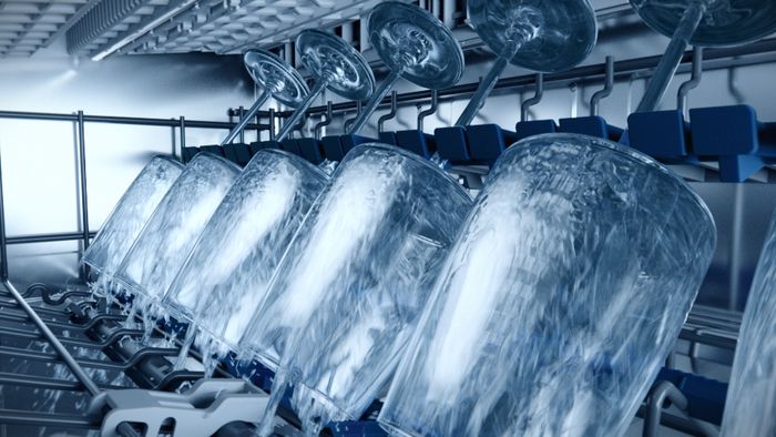 בתמונה מוצגות כוסות זכוכית שמסתובבות במדיח כלים, כשהן ממוקמות על מדף מיוחד. נראה כאילו מים זורמים על הכוסות, מה שמעיד על תהליך ניקוי פעיל, כנראה עם לחץ מים גבוה. המדיח מתפקד בצורה יעילה לשטוף את הכלים.