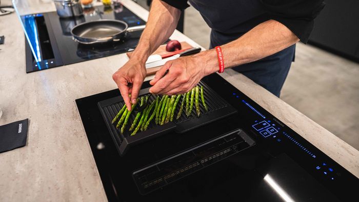 A man grills asparagus on a venting hob, showcasing vibrant green spears cooking over an open flame.  