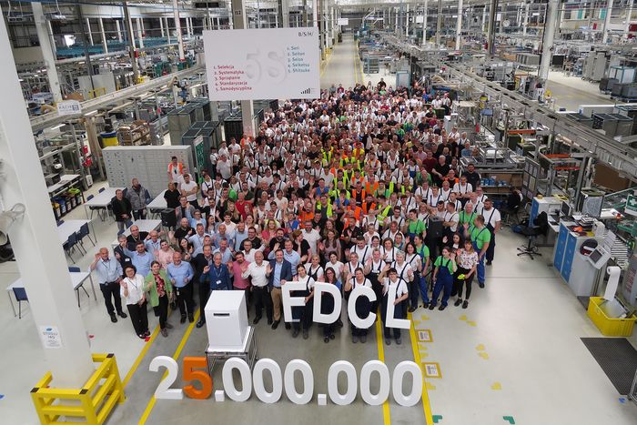 Zdjęcie grupowe pracowników fabryki, na tle lini produkcyjnych.