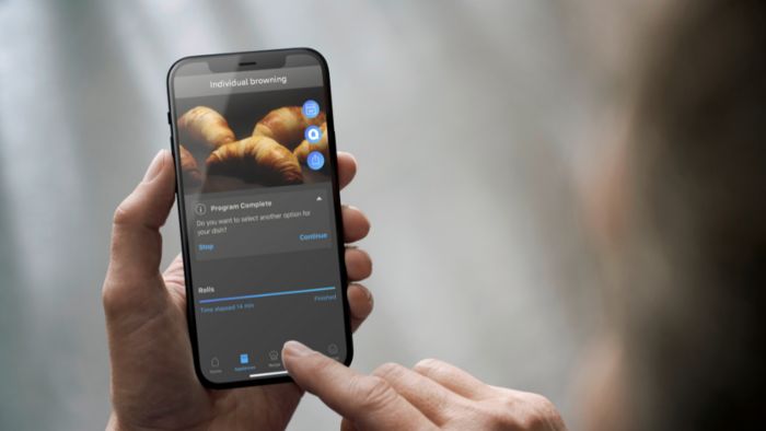 יד של אדם אוחז במכשיר סלולרי ולוחץ על אפליקציית הום קונקט שמתחברת לתנור של סימנס
