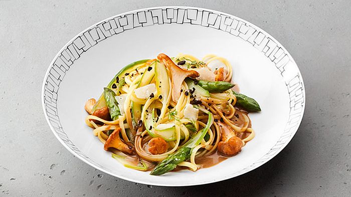 Bord met linguine-pasta met paddenstoelen en groene asperges.