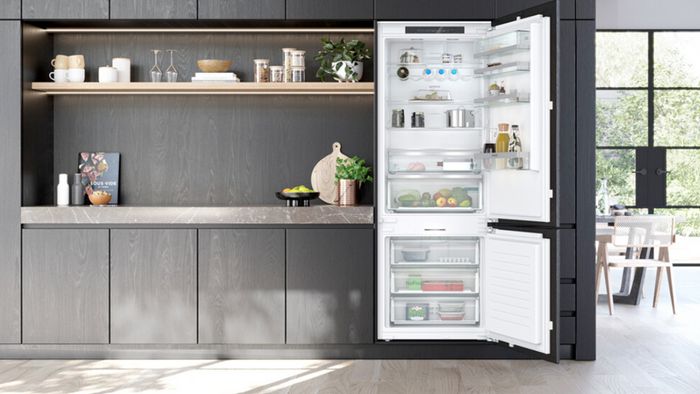 Cocina moderna e iluminada de madera oscura con un frigorífico integrable Siemens abierto lleno de alimento.