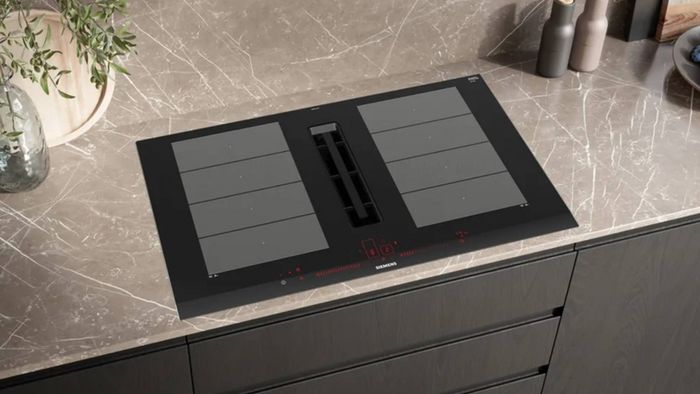 Placa de inducción Siemens de diseño moderno, integrada en una encimera de piedra, con controles táctiles y diseño elegante.