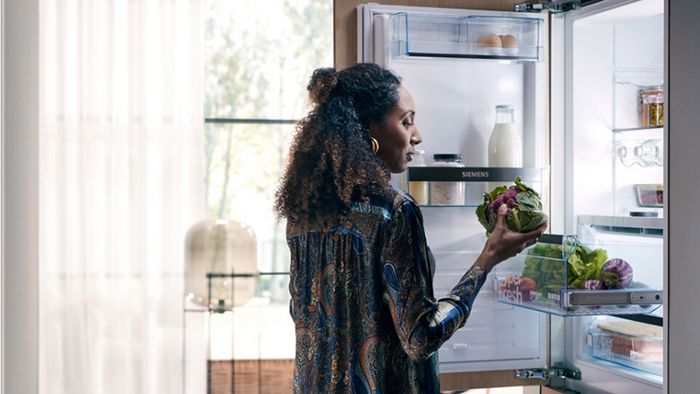 Mujer cogiendo alimentos de un frigorífico integrable Siemens en una cocina moderna e iluminada. 