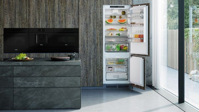 Frigorífico integrable Siemens en cocina moderna, puerta abierta, isla con encimera de mármol gris y electrodomésticos negros.