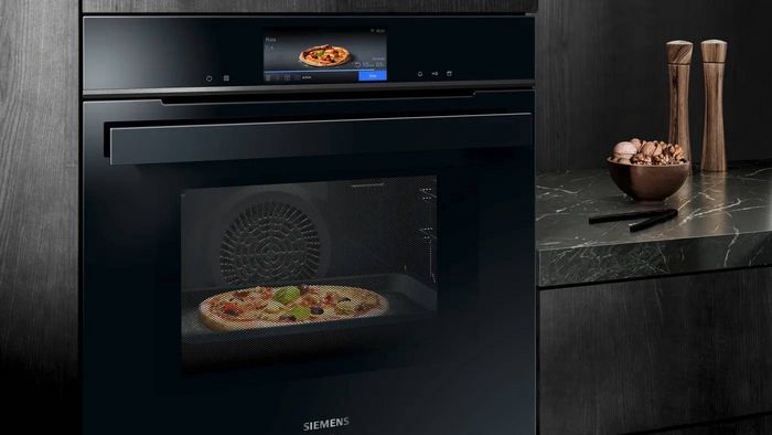 Horno Siemens negro empotrado en cocina moderna con pared de madera oscura y encimera de m&aacute;rmol. 