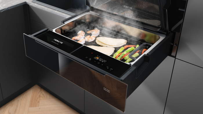 Siemens studioLine Dampfschublade mit geöffnetem Fach, gefüllt mit Gemüse, Fisch und Garnelen beim Dampfgaren in moderner Einbauküche.