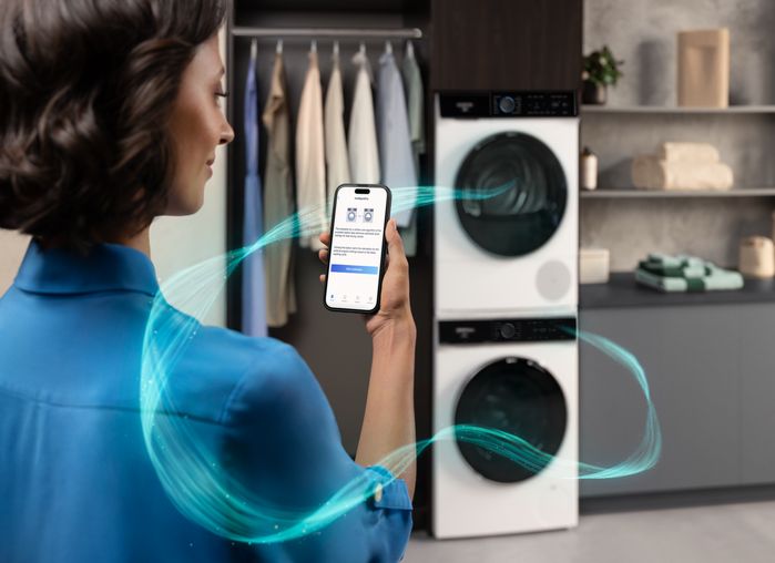 Donna che controlla l&rsquo;app per la gestione del bucato su smartphone davanti a una colonna lavatrice e asciugatrice Siemens