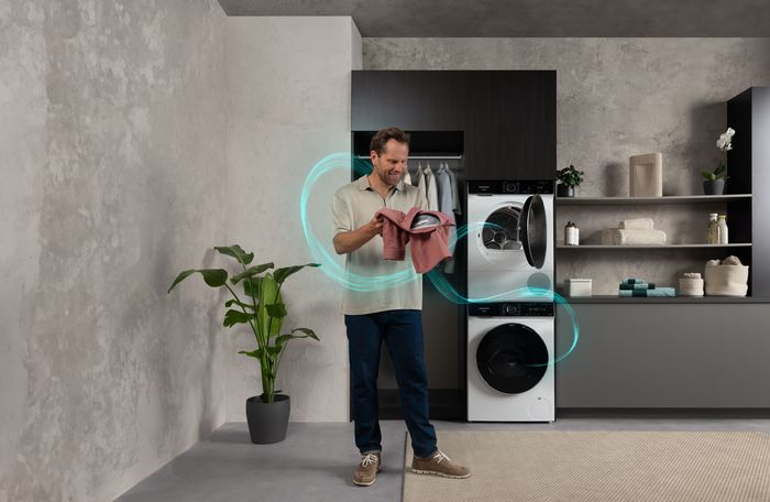 Een man houdt een roze overhemd vast voor een moderne Siemens iQ700-wasmachine en -droger.       