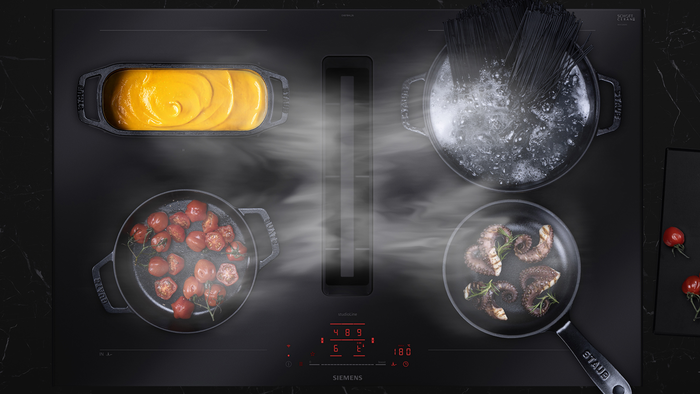Siemens Induktionskochfeld mit dampfenden Töpfen und Pfannen, in denen Speisen gegart werden.